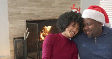 Şöminenin yanındaki koltukta Noel Baba şapkası takan, başını omzuna dayayıp gülen bir kadın. Samimiyet, samimiyet, sıcaklık, kutlama, dostluk, şefkat, şenlik