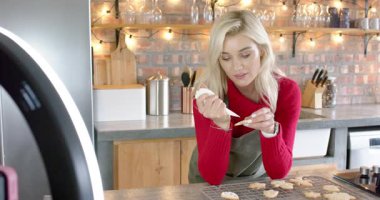 Önlüklü bir kadın mutfak tezgahında krema borularına krema sıkıyor ve tekniği anlatıyor. Pişirme, şekerleme, işçilik, yemek tasarımı, aşçılık, stil, detay odaklı