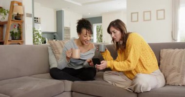 Çeşitli bayan arkadaşlar ekran dinleyicisine tepki veriyor, telefonu kaydırıyor ve kanepede kupalarla gülüyorlar. Arkadaşlık, rahatlama, sosyalleşme, samimi, samimi, modern, konuşkan