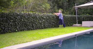 Bahçe botlarıyla yeşillikler, hasat eden ve havuz kenarını budayıp işaret eden kadın arkadaşlar. Bahçe işleri, takım çalışması, açık hava, eğlence, doğa, peyzaj, işbirliği