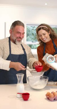 Dikey video: kek için mutfakta kevgir tutan ve un döken çift. Mutfak eşyaları, ev eşyaları, ev yapımı, pişirme, aşçılık, dikey video