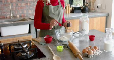 Mutfak tezgahında kırmızı kaşık ve şişe kullanan bir kadın, kabın içine özütü koyup karıştırıyor. Pişirme, aşçılık, hamur işi, kırsal, ev yapımı, beslenme, hassasiyet