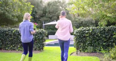 Çimenlerde pembe tencereler taşıyan, diz çökmüş çiçek açan, bahçeyi güzelleştiren dişi arkadaşlar. Bahçıvanlık, arkadaşlık, açık hava, çiçek, peyzaj, boş zaman, doğa.