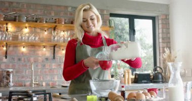 Kırmızı süveter giyen, hamuru mutfaktaki kırmızı ölçü kabına döken tam bir tarif ölçüsü. Aşçılık, aşçılık, ev, ev, iç mekan, mutfak eşyaları, yaşam tarzı