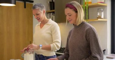 Anne ve kızı, yemek tarifini takip ediyor. Mutfak adasında süzme ve eleme yapıyorlar. Aile, işbirliği, evcil, rahat, pişirme, gelenek, sade