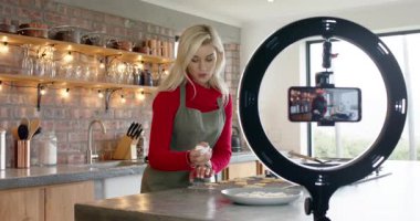 Kadın pasta poşetinden kurabiyeye kadar krema sıkıyor ve demo için akıllı telefon çekiyor. Pişirme, tatlı, şekerleme, aşçılık, içerik oluşturma, yaşam tarzı, konforlu