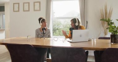 Çeşitli kadın sunucular evdeki yayını kaydeden mikrofona konuşan eşlerine doğru dönüyorlar. İşbirliği, iletişim, podcast, modern, gündelik, dostane, profesyonel