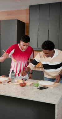Dikey video: Erkek arkadaşlar telefon tarifi okurken sos dağıtırken, mutfak barında peynir yerken. İşbirliği, aşçılık, modern, enerjik, takım çalışması, hazırlık, dikey video