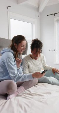 Dikey video: Telefon ekranı çeşitli bayan arkadaşlarını yatakta gülen direklerle baş sallamaya teşvik ediyor. Arkadaşlık, rahat, rahat, yaşam tarzı, modern, eğlence, dikey video