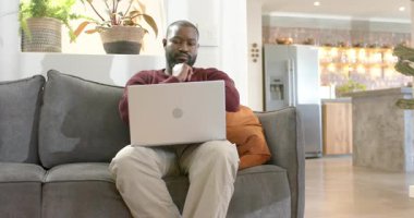 Çenesini destekleyen Afro-Amerikalı bir adam. Sonra gümüş dizüstü bilgisayarla evde ders çalışıyor. Konsantrasyon, üretkenlik, modern, yerli, çalışma alanı, teknoloji, rahatlama