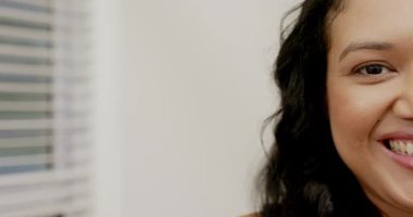 20 'li yaşların ortalarında bir kadın kamerayı odada karşılıyor. Panjurlara ve beyaz duvara gülümsüyor. Kopya uzayı. Portre, sağlık, sakinlik, dinginlik, minimalizm, zarafet, doğal ışık