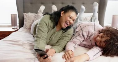 Akıllı telefon içeriğini, çeşitli anne ve genç kızın gülüşünü, yatakta lamba üstüne kaydırışını görmek. Aile, bağ, bağ, rahatlama, konfor, yaşam tarzı, samimiyet