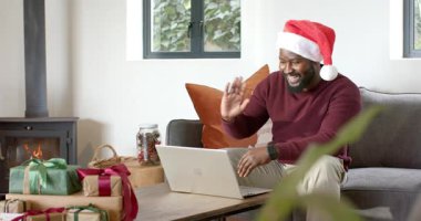 Dizüstü bilgisayara odaklanmış, evde tatil sırasında el sallayan Afrikalı Amerikalı orta yaşlı bir adam. Şen, samimi, kutlama, ev, dijital, iletişim, mevsimlik