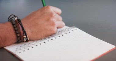 Adam yeşil kalemle çerçeveye uzanıp deftere yazarak kırmızı kaplamalı akıllı telefonu masaya yerleştiriyor. Yaratıcı çalışma, kırtasiye, yazı, not alma, minimalist, çalışma alanı, üretkenlik