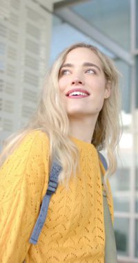 Dikey video: Sırt çantalı, mavi kayışlı bir kadın binanın tepesine doğru eğilmiş. Kentsel, mimari, modern, düşünceli, gündelik, yaşam tarzı, dikey video