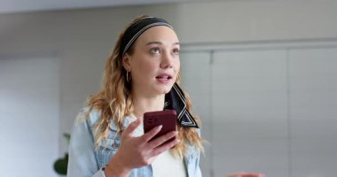 Akıllı telefon tutan, alnını gölgeleyen, okuma alıştırması yapan, evinde saksı bitkisinin yanında el kol hareketi yapan bir kadın. Teknoloji, iletişim, anlamlı, gündelik, yaşam tarzı, iç mekan, sağlık