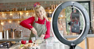 Kadın mutfak tezgahındaki kasede bayram sütü için yumurta çırparken kamerayı selamlıyor. Mutfak, yaşam tarzı, minimalist, yemek pişirme, yerli, neşeli, besleyici