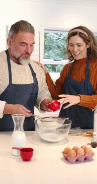 Dikey video: Bir çift mutfakta metal elek ile un ellemeden önce kırmızı bardak alıyor. Mutfak, ev yemeği, yemek pişirme, birliktelik, konforlu, yerli, dikey video