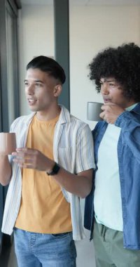 Dikey video: Çeşitli erkek arkadaşlar yeşilliği göstererek bardakları alıyor ve gülüyorlar. Arkadaşlık, dostluk, rahatlama, bağlantı, konukseverlik, modern, dikey video