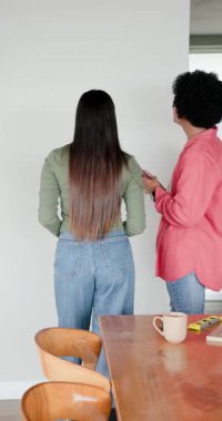 Dikey video: Telefon kullanan, çivi çakan ve yemek duvarındaki çerçeve seviyesini kontrol eden farklı bir çift. Ev geliştirme, diy, işçilik, işbirliği, modern, samimi, dikey video