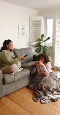 Dikey video: Anne akıllı telefona bakıyor evde haberleri taraması için kızına telefon teklif ediyor. Aile, bağ, rahatlama, rahatlama, iletişim, yaşam tarzı, dikey video