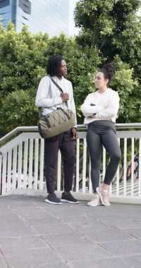 Dikey video: korkuluktaki çeşitli arkadaşlar, spor çantalı adam sohbete başlıyor ve kadın başını sallıyor. İşbirliği, ağ oluşturma, kentsel çevre, yaşam tarzı, modern, bağlantı, dikey video