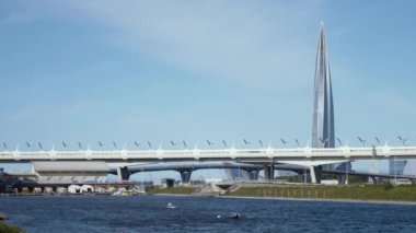 İnsanlar bir köprü ve gökdelenin arka planına karşı kürek çekiyor. Şehrin arka planında teknelerde insanlar var..