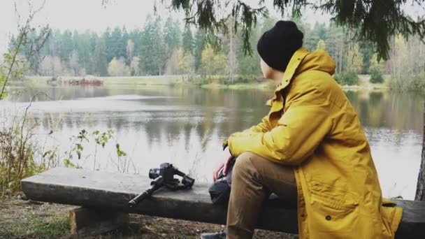 Homem Senta Junto Lago Num Banco Lado Uma Árvore Fotógrafo — Vídeo de Stock