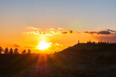 Gün batımına karşı ağaç tepeleri. Güneşin turuncu ışınları Noel ağaçlarının ve çam ağaçlarının dallarından görülebilir.. 