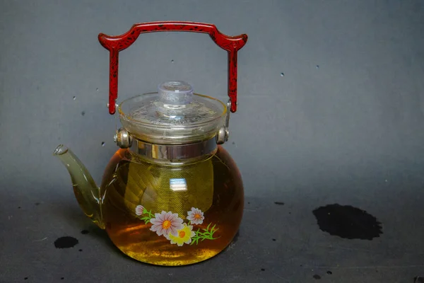 A kettle with a red handle, next to pressed green tea with mint. Tea party.