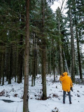 Parlak sarı ceketli bir adam arkası dönük duruyor. Güzel, soğuk bir kış ormanının arka planına karşı. Kar ve buz ayak altında yatıyor. Vahşi doğadaki adam.