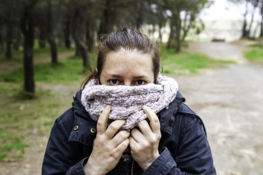 Ormanda fularlı ve soğuk tabadalı bir kadın, fırtınalı bir hava.