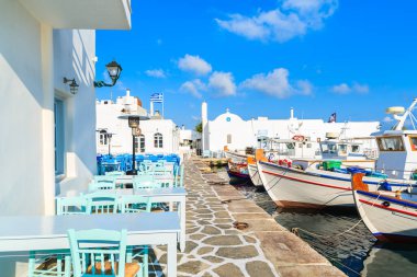 Yunanistan 'ın Paros adasındaki Naoussa limanında bar masaları ve geleneksel balıkçı tekneleri