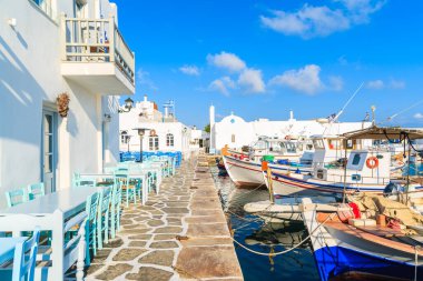 Yunanistan 'ın Paros adasındaki Naoussa limanında bar masaları ve geleneksel balıkçı tekneleri