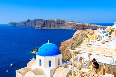 OIA VILLAGE, SANTORINI ISLAND - 23 Mayıs 2016: Yunanistan 'ın Santorini adası, mavi kubbeli beyaz kiliseleriyle tanınan ünlü Oia köyünde kız arkadaşının fotoğrafını çeken genç adam.