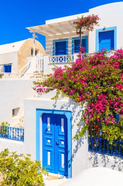 Yunanistan 'ın Santorini adasındaki Oia köyünde kırmızı çiçeklerle süslenmiş tipik beyaz ve mavi Yunan evi