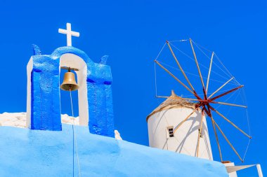 Yunanistan 'ın Santorini adasındaki Oia köyünde tipik bir Yunan kilise kulesi ve mavi arka planda bir yel değirmeni