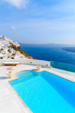 Yunanistan 'ın Santorini adasındaki Imerovigli köyünün tipik beyaz mimarisi, ön planda kaldera ve lüks yüzme havuzu manzarası.