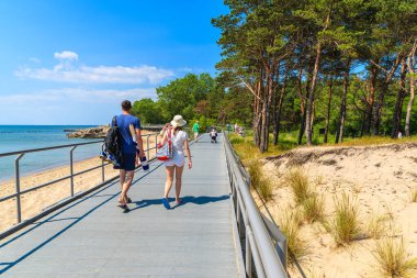 HEL, BALTIC SEA - 22 Haziran 2016: Polonya 'nın Baltık Denizi kıyısındaki Hel kasabasında sahil boyunca yürüyen iki turist. Hel yarımadası yaz tatilleri için popüler bir yerdir..