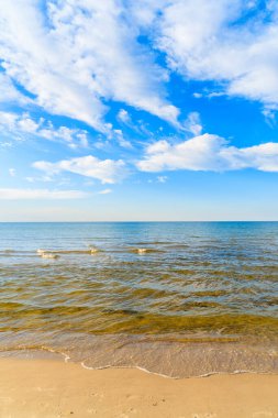 Kumlu sahilde deniz dalgaları ve mavi gökyüzünde beyaz güneşli bulutlar Baltık Denizi, Polonya 'da Debki köyünde