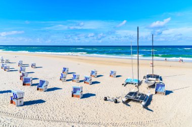 Güneşli bir yaz gününde Kampen sahilinde, Kuzey Denizi, Almanya 'daki Sylt Adası' nda hasır sandalyeler ve yelkenli tekneler.
