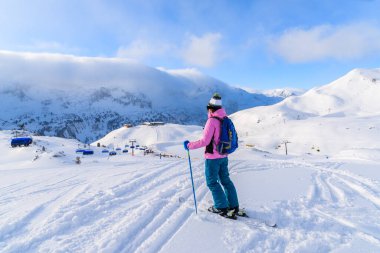 Genç bayan kayakçı taze karda duruyor ve Avusturya 'nın Obertauern kayak alanındaki dağlara bakıyor.
