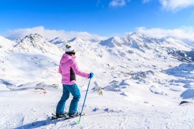 Genç bayan kayakçı Avusturya 'nın Obertauern şehrinde kayak pistinde karlı dağlara bakıyor.