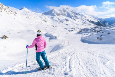 Genç bayan kayakçı Avusturya 'nın Obertauern şehrinde kayak pistinde karlı dağlara bakıyor.