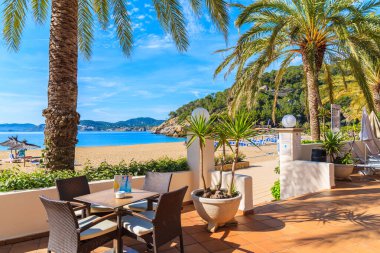 CALA SAN VICENTE BAY, IBIZA ADASI - 17 Mayıs 2017: Cala San Vicente Körfezi, İbiza Adası, İspanya 'da palmiye ağaçları olan plajdaki bar masaları.