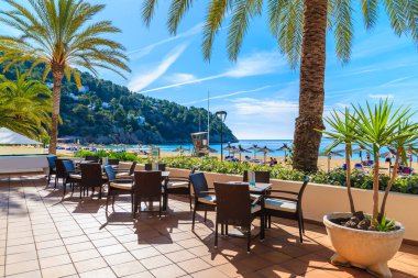 İspanya 'nın İbiza adasındaki Cala San Vicente Körfezi' nde palmiye ağaçları olan sahildeki bar masaları terasında.
