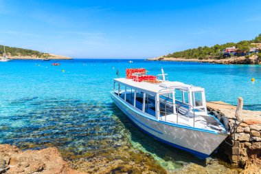 İspanya 'nın İbiza adasındaki Cala Portinatx Körfezi' nde demirleyen turistler için beyaz ve mavi feribot.