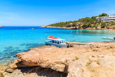 İspanya 'nın İbiza adasındaki Cala Portinatx Körfezi' nde demirleyen turistler için beyaz ve mavi feribot.
