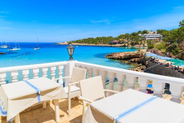 CALA PORTINATX, IBIZA ISLAND - 22 Mayıs 2017: Cala Portinatx Koyu, İbiza Adası, İspanya 'daki sahil restoranının terasında sandalyeli masalar.