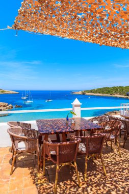 İspanya 'nın İbiza adasındaki Cala Portinatx Körfezi' ndeki sahil restoranının terasında sandalyeli masalar..